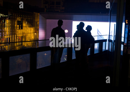 Quattro giovani in piedi su un balcone in un centro commerciale per lo shopping di notte nel quartiere di Sanlitun della centrale di Pechino, Cina. Foto Stock