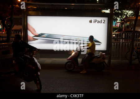 Un uomo su uno scooter motorizzato passando un annuncio per un Apple iPad nel quartiere di Sanlitun della centrale di Pechino, Cina. Foto Stock