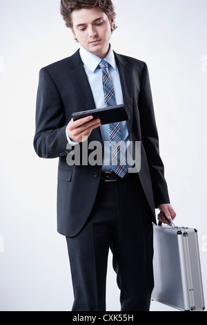 Giovane Imprenditore guardando a tavoletta digitale e VALIGETTA TRASPORTO Foto Stock