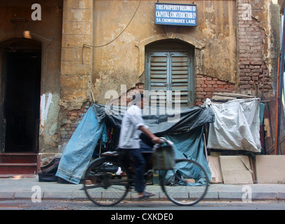 Ciclista passa improvvisato negozio in un quartiere povero di Kolkata (Calcutta) la capitale dello stato indiano del Bengala Occidentale. Foto Stock