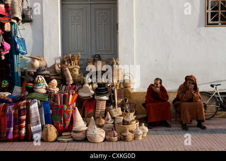 Due uomini marocchini seduto fuori dal negozio di vendita ceste, panni e negozio di souvenir a Essaouira, Marocco Foto Stock