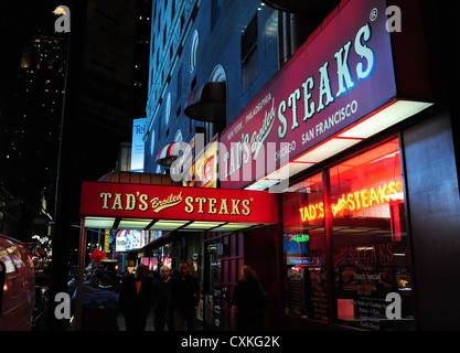 Neon di notte vista obliqua verso la settima Avenue, la gente camminare sul marciapiede tendone rosso del Tad bistecche, West 50th Street, New York Foto Stock