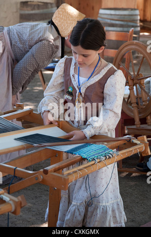 Ragazza giovane docente nel periodo di funzionamento del vestito di un telaio di tessitura a Sutter's Fort State Historical Park a Sacramento, in California. Foto Stock