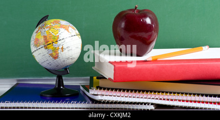 Mini globe, Apple, spirali e libri di fronte a una lavagna verde Foto Stock