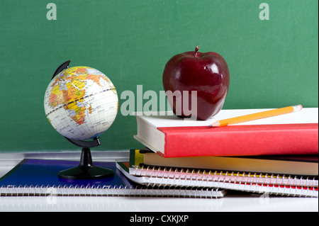 Un mini globe, Apple Notebook a spirale e i libri di testo di fronte a una lavagna verde Foto Stock