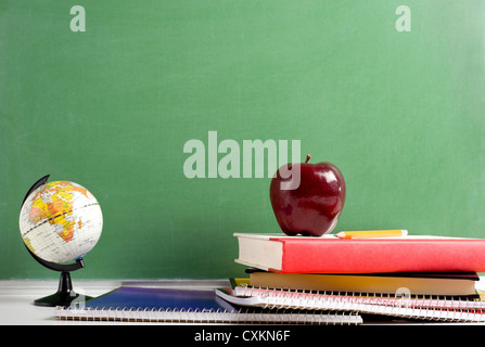 Un mini globe, Apple Notebook a spirale e dei libri di testo di nuovo una lavagna verde con spazio di copia Foto Stock