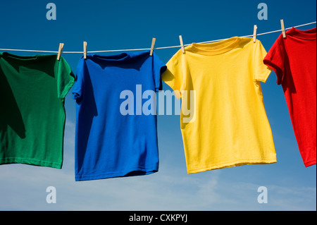 Una riga del file colorate di t-shirts appeso su appendiabiti su un cielo blu sullo sfondo Foto Stock