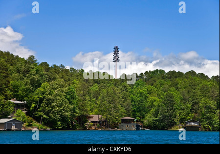 Una torre cellulare ad alta al di sopra della linea di albero in case e un lago. Foto Stock