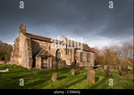 Esterno del soleggiato storica Chiesa di Tutti i Santi & sagrato lapidi in una tranquilla zona panoramica campagna sotto il cielo scuro, Weston, North Yorkshire, Inghilterra, Regno Unito Foto Stock
