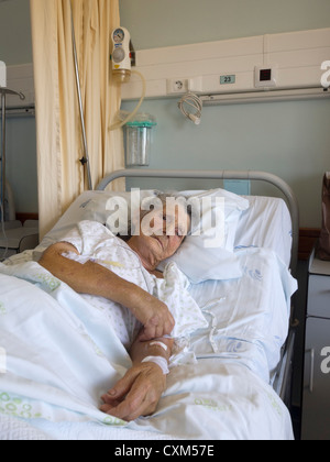 Donna anziana giacente sul suo letto in un ospedale Foto Stock