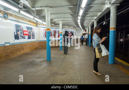 New York, New York, Stati Uniti, persone in attesa del treno sul binario di Bleecker Street, stazione della metropolitana di New York, Manhattan, donna telefonare a new york DA SOLA al suo interno Foto Stock