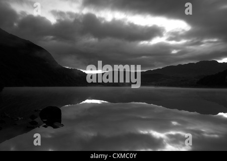 Moody nuvole grigie riflettono in acqua ancora di un lago, Llyn Dinas, Wales, Regno Unito Foto Stock