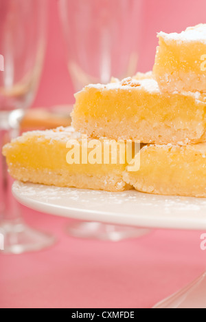 Deliziosi appena sfornato piazze di limone su una torta bianca stand con bicchieri di champagne in background Foto Stock