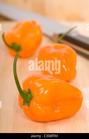 Tre Habanero peppers su un tagliere con un coltello in background Foto Stock