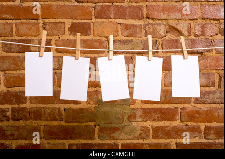 Una fila di cinque note vuote su stendibiancheria di fronte a un muro di mattoni, con spazio di copia Foto Stock