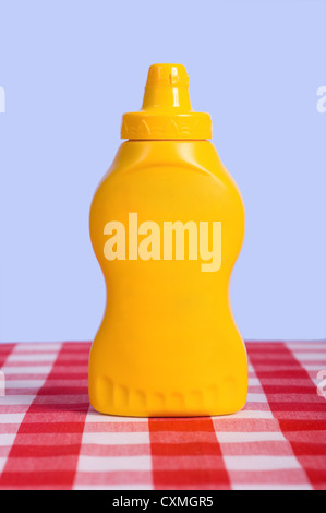 Un giallo squeeze bottiglia nella parte anteriore di un cielo blu su bianco e rosso controllato o tovaglia gingham con nessuna etichetta