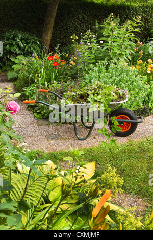 Per ripulire il giardino estivo pieno di fiori e la carriola con giardino-rifiuti, piante ed erbe infestanti - verticale, Foto Stock