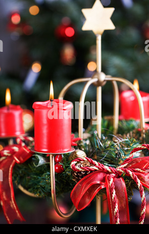 Corona di avvento con la masterizzazione di candele rosse, albero di Natale sullo sfondo Foto Stock