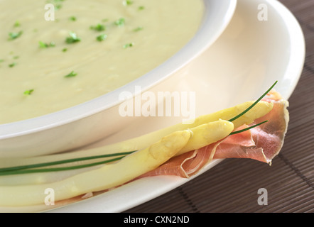 La crema di asparagi bianchi guarnite con prezzemolo e asparagi bianchi, prosciutto ed erba cipollina sul cerchione Foto Stock