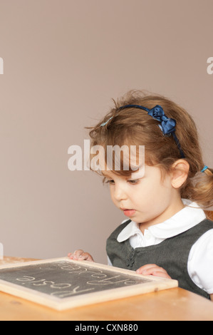 4 anno vecchia ragazza in uniforme scolastica pratica di scrittura su una piccola scheda di gesso. Foto Stock