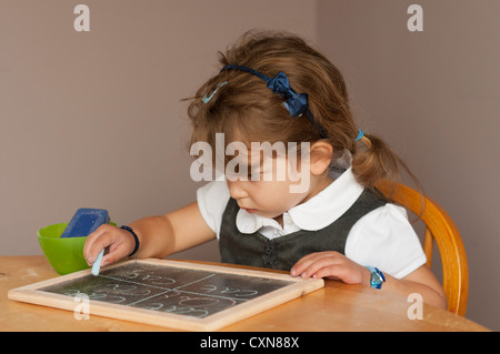 4 anno vecchia ragazza in uniforme scolastica pratica di scrittura su una piccola scheda di gesso. Foto Stock