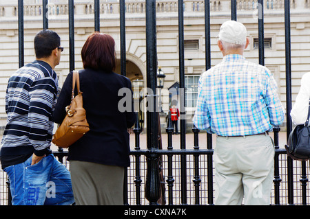 I turisti alla ricerca attraverso le ringhiere fuori Buckingham Palace. Foto Stock