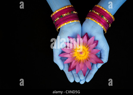 Ragazza indiana offre un Nymphaea tropicale Fiore di ninfea blu con mani dipinte e bracciali contro uno sfondo nero Foto Stock