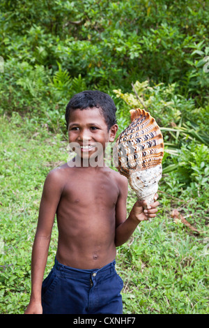 Indonesia, Papua Nuova Guinea, Kitava isola. Ragazzo giovane azienda grandi triton shell. Foto Stock