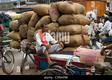 Driver Cyclecart davanti a un carrello impilati con sacchi di tela su Khari Baoli Road, (Spice Market Bazar off Chandni Chowk), la Vecchia Delhi, India Foto Stock