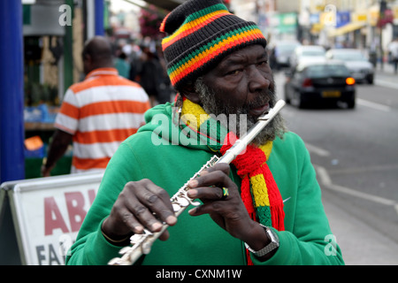 Flautista flutewise giocando a Londra, nel vibrante rastafarian i colori indossando bandiera giamaicana anello da dito, tre piccoli uccelli. Foto Stock