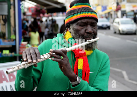 Flautista flutewise giocando a Londra, nel vibrante rastafarian i colori indossando bandiera giamaicana anello da dito, tre piccoli uccelli. Foto Stock