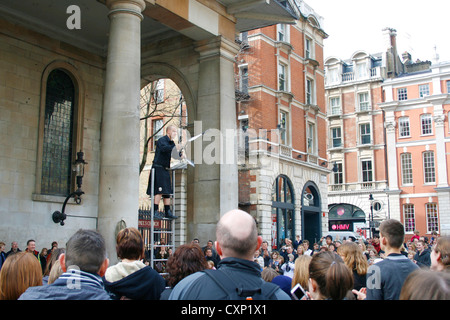 Un uomo di giocoleria sorgeva su una coppia di scale divertente la folla di persone al Covent Garden di Londra England Regno Unito. Foto Stock