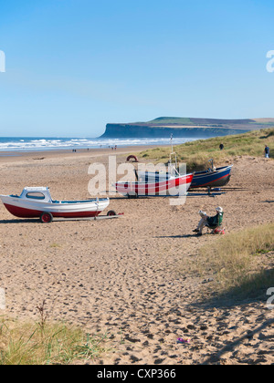 Su un soleggiato autunno domenica pomeriggio un uomo legge un giornale per le barche di pescatori sulla spiaggia di Marske Foto Stock