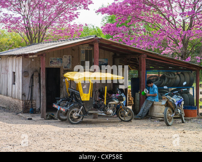Un uomo si siede accanto alla sua moto pedicab davanti ad una modesta casa nel Chaco paraguaiano. Foto Stock