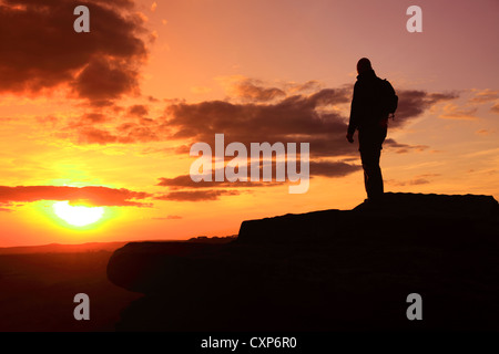 Uomo adulto camminatore con zaino che guarda il tramonto sul bordo di Curbar, il Peak District National Park, Derbyshire Foto Stock