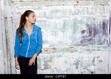 Donna che indossa abiti sportivi in piedi contro un muro in una tuta blu top Foto Stock