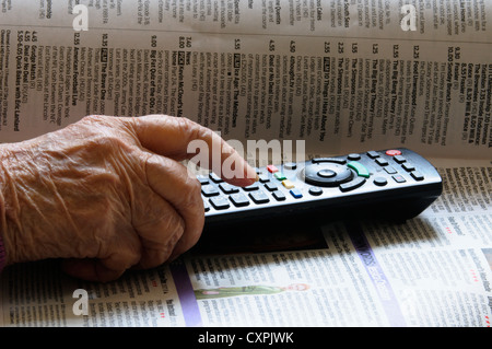 Signora anziana che usa un telecomando televisivo e una guida ai programmi TV. Senior che utilizza la tecnologia attuale. Foto Stock