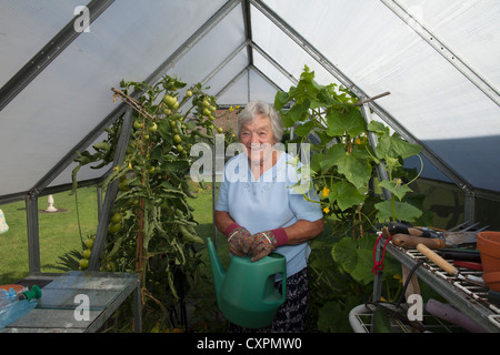 Donna anziana tendendo le piante in serra Foto Stock