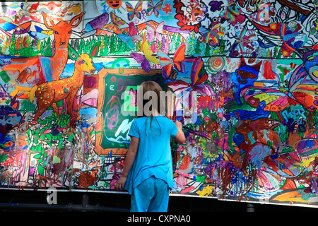 Giovane ragazza in piedi di fronte a un grande murale ella è dipinto su alla Moss Street di vernice-in. Un esterno art show e la vendita in vi Foto Stock