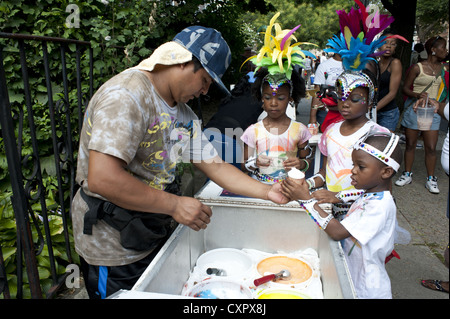 USA: Brooklyn, New York. I bambini in costume acquistare ices durante dei Caraibi Kiddies parata del giorno, Crown Heights, 2012. Foto Stock