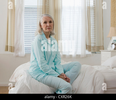 Ritratto di triste senior donna seduta sul letto indossando pigiami Foto Stock