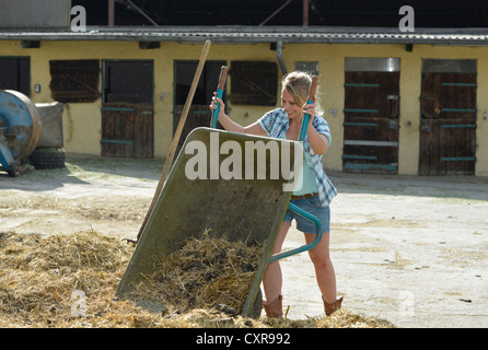 Femmina giovane agricoltore, letame equino, pulizia, spingere il carrello, carriola, Gingen, Baden-Wuerttemberg, Germania, Europa Foto Stock