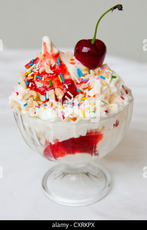 Una foto a colori di un gelato alla fragola in una ciotola di vetro con un pizzico e una ciliegina sulla torta. Foto Stock