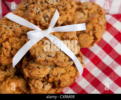 Immagine a colori di Chocolate Chip Cookie Avena legati insieme con un nastro bianco. Impostare contro un bianco e rosso tovaglia controllati Foto Stock