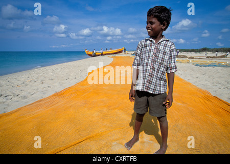 Il ragazzo, figlio di un pescatore, in piedi su una pesca gialla net nella parte anteriore di una barca da pesca, Adam's Bridge Foto Stock