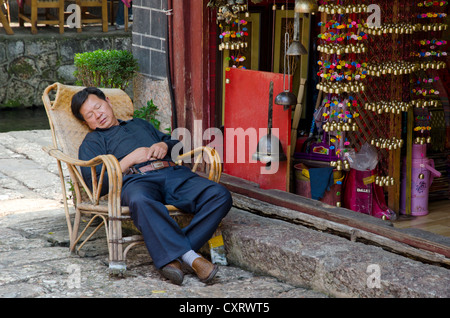 Negoziante addormentato nella parte anteriore del suo negozio Lijiang, Yunnan, sud-est della Cina, la Cina, Asia Foto Stock