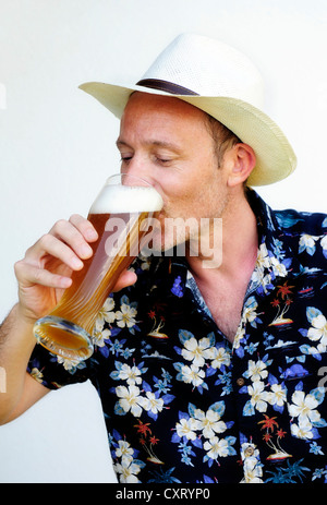 Uomo che indossa un cappello di paglia e una camicia hawaiana di bere birra di grano Foto Stock