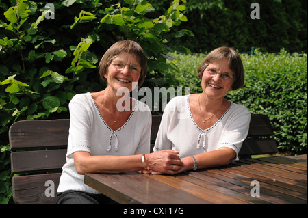 Due vispo gemelle seduta su una panchina Foto Stock