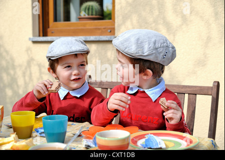 Twin boys, 4, indossando tappi piatte, sedersi e mangiare in una tabella Foto Stock