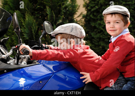 Twin boys, 4, indossando tappi piatti seduti insieme su un motociclo blu Foto Stock